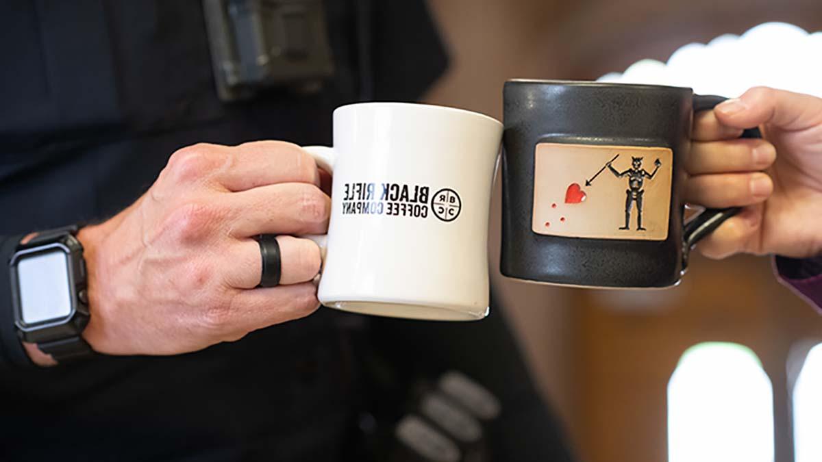 Two veterans hold coffee mugs with logos from the Black Rifle Coffee Company.