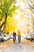 Two students ride down Greek Row 在 fall, amid changing leaves.